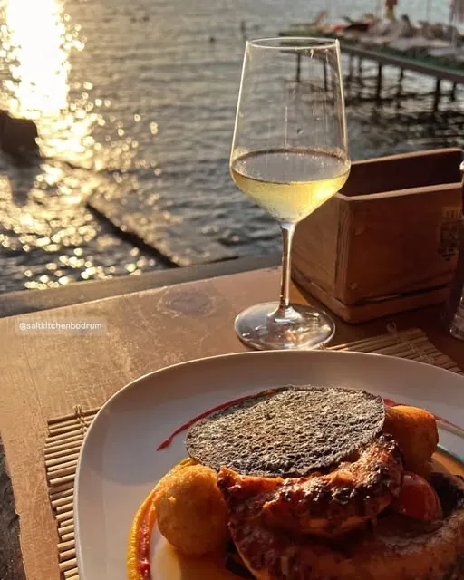 A dish and white wine right on the water at golden hour